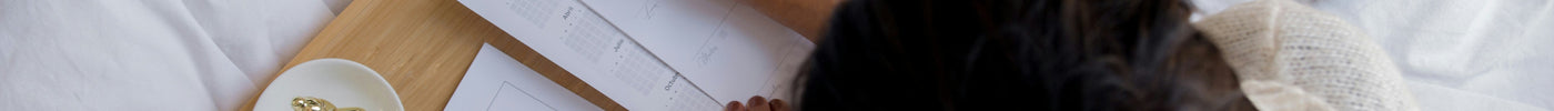 Woman writing her daily plans in bed with a cup of coffee using planner pages from The Planner Shop